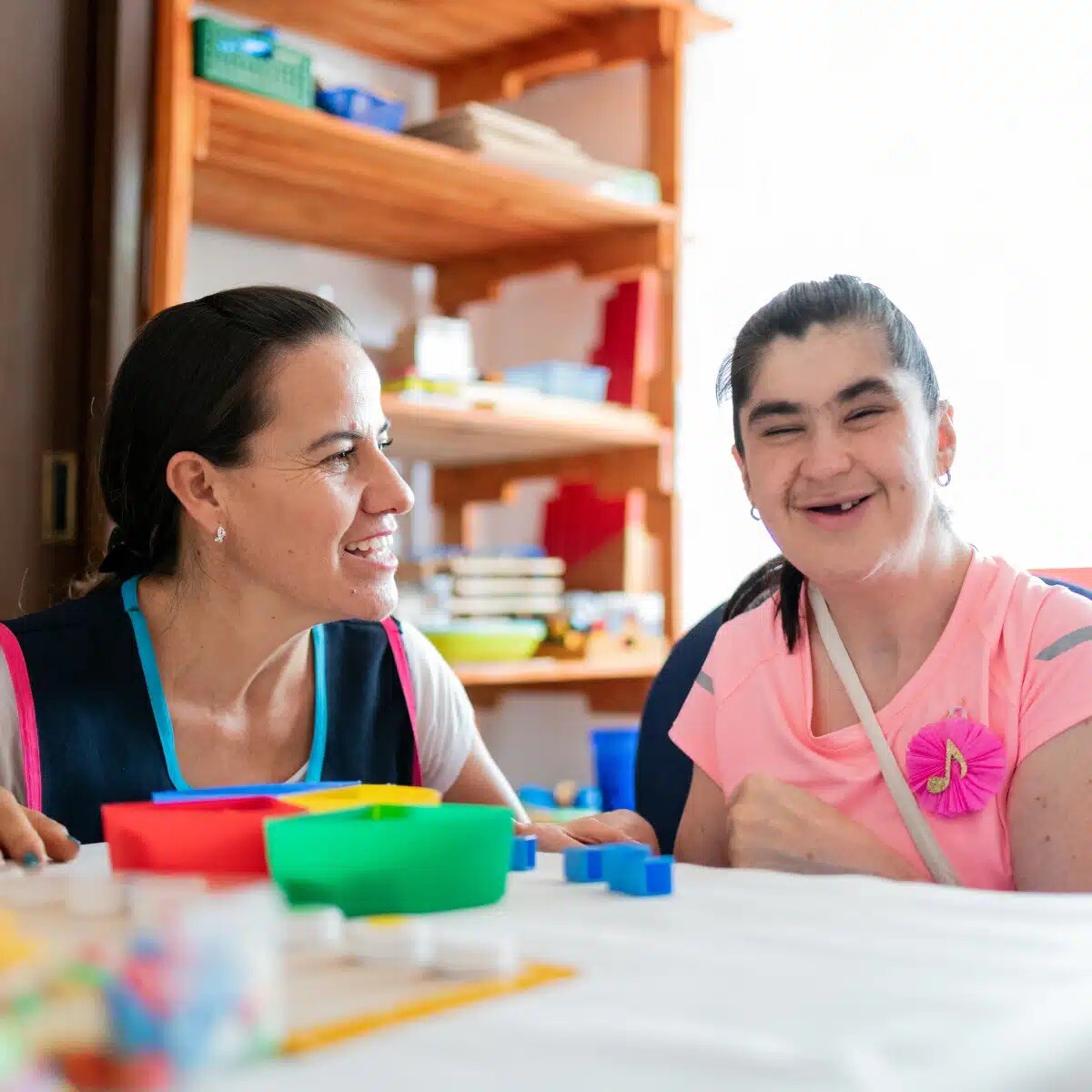 A woman and a young girl sit at a table, smiling, playing with building blocks. A woman and a young girl sit at a table, smiling, playing with building blocks.