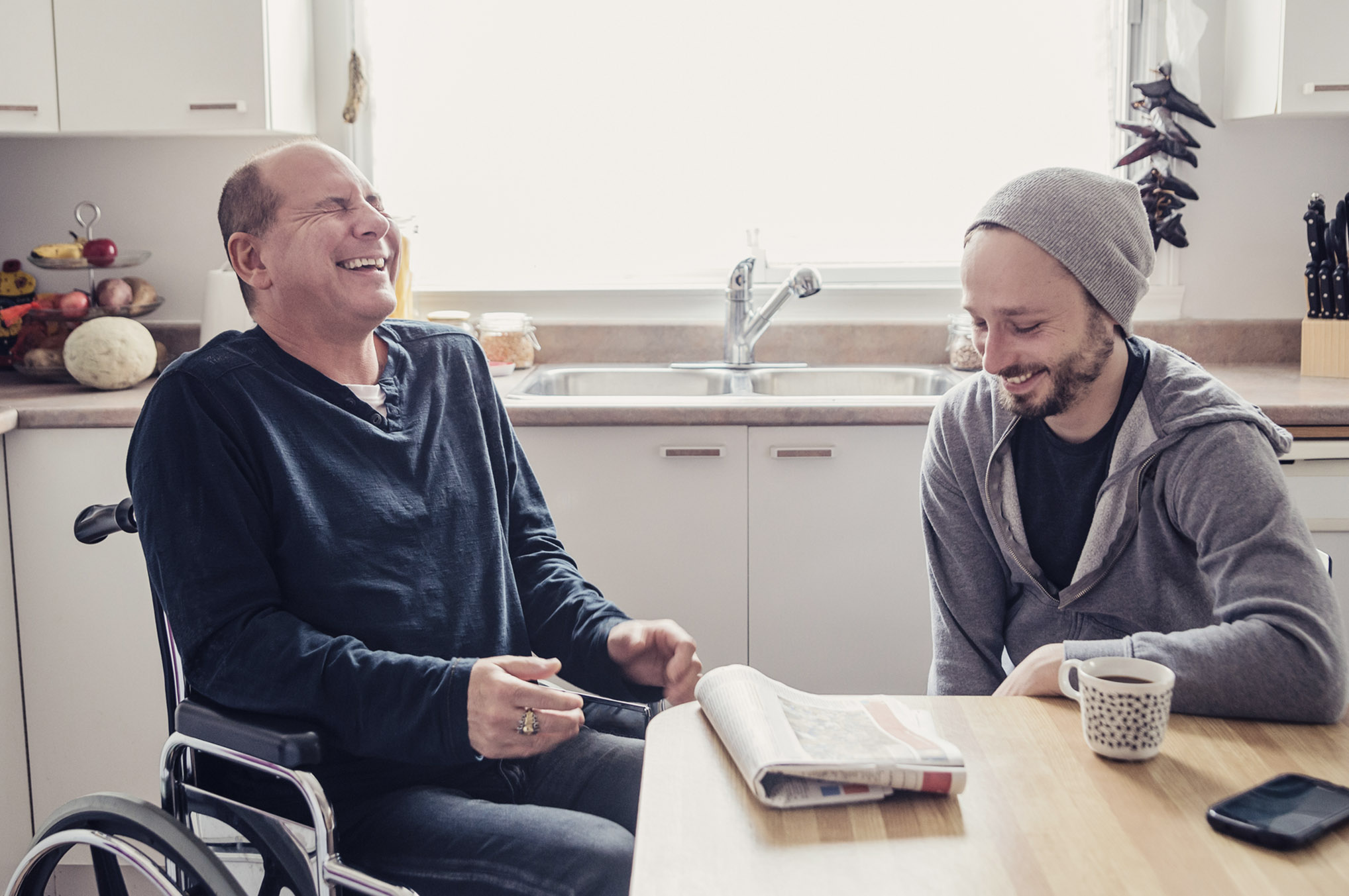 A man in a wheelchair sits beside another man, both engaged in a friendly conversation. A man in a wheelchair sits beside another man, both engaged in a friendly conversation.